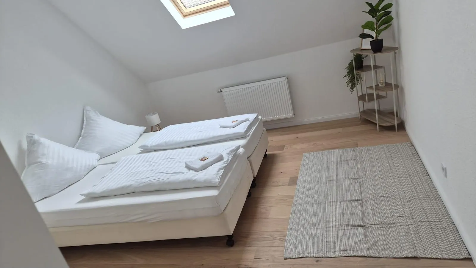 Schlafzimmer einer Ferienwohnung mit frisch bezogenen Betten unter dem Dachfenster