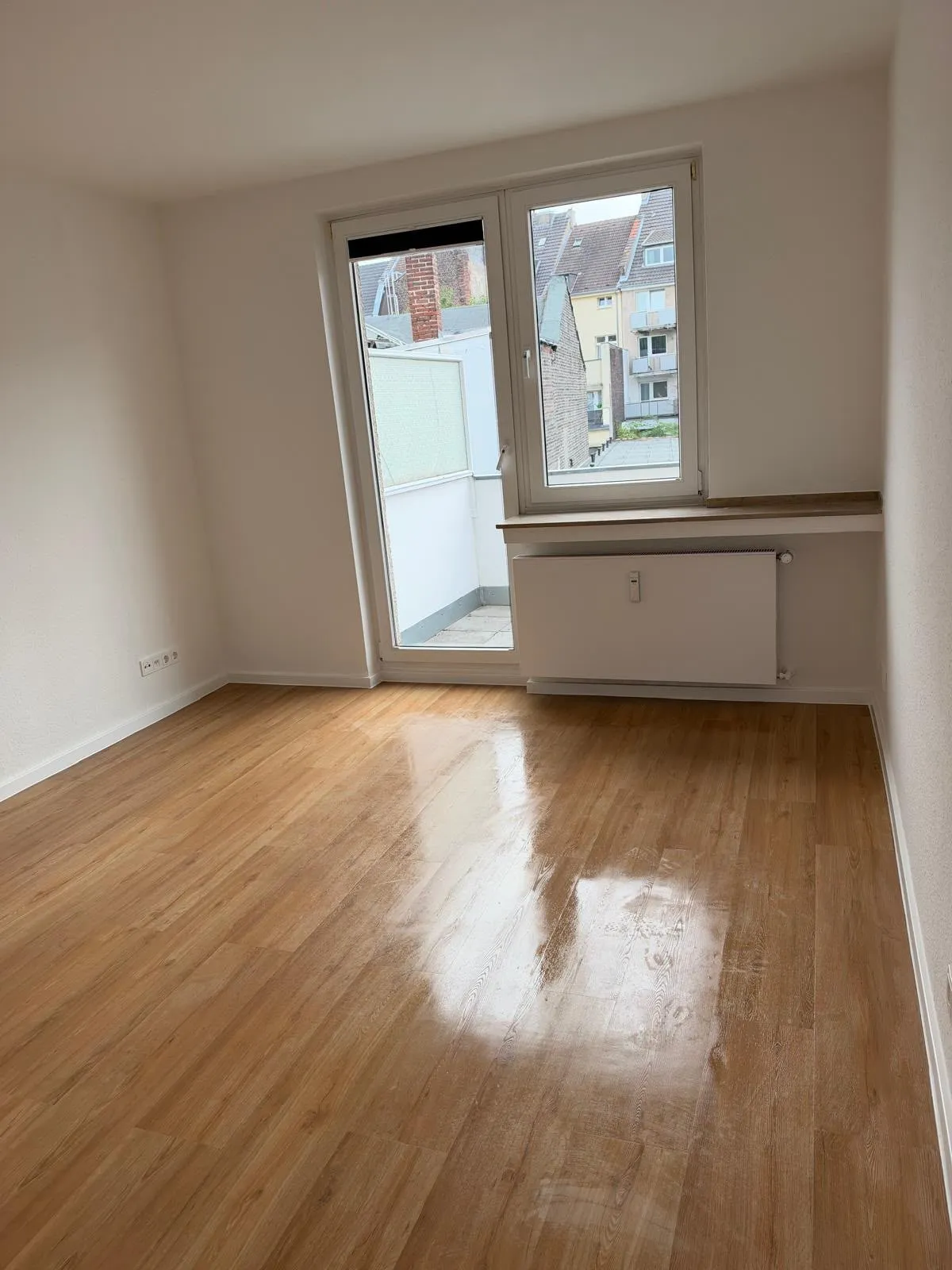 Leeres Zimmer mit Balkontür und frisch gewischtem, glänzendem Boden